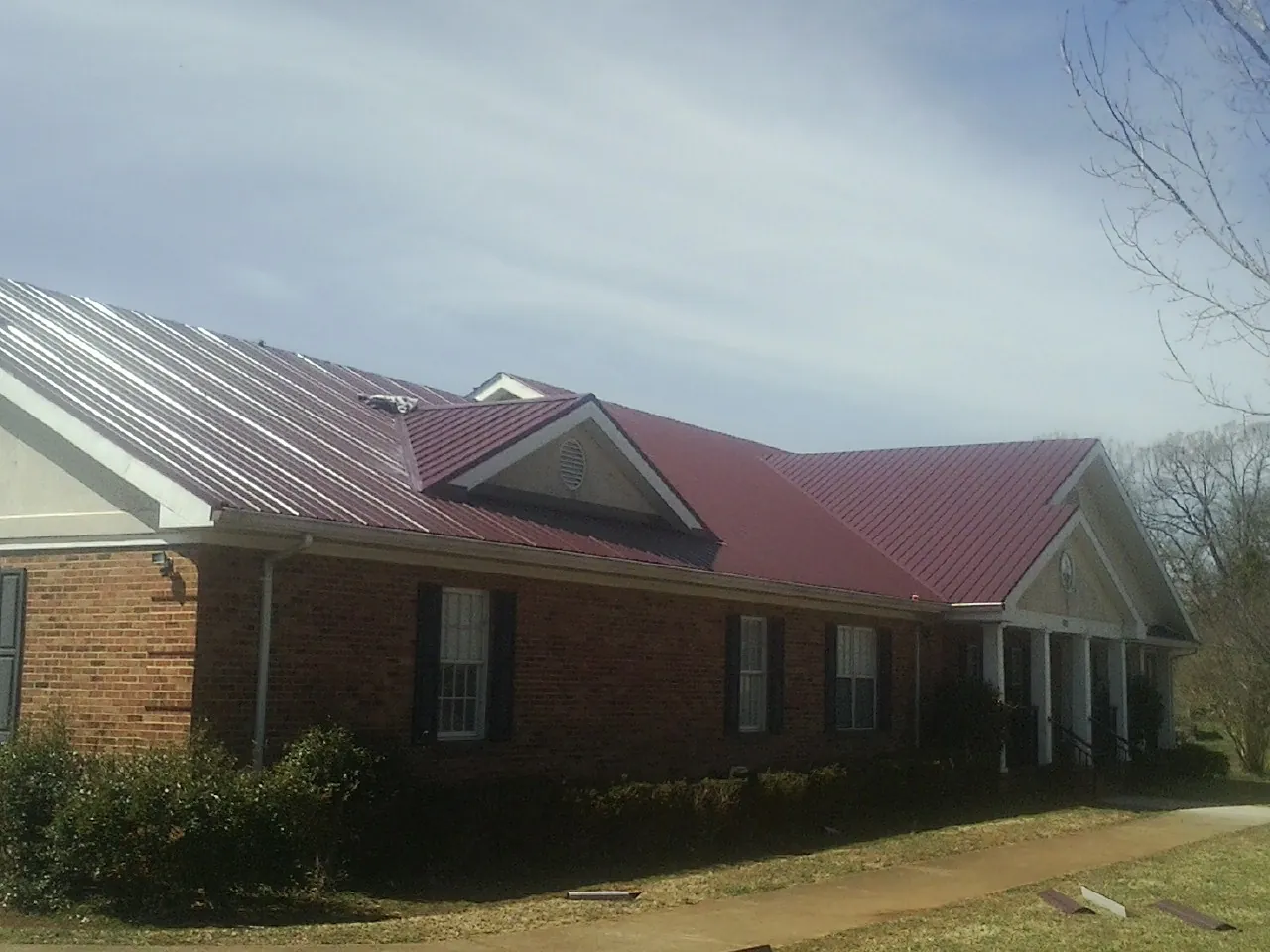 Red metal roof with gabled entries on a long brick building, from a Hail Damage Roof Repair job in Thorndale