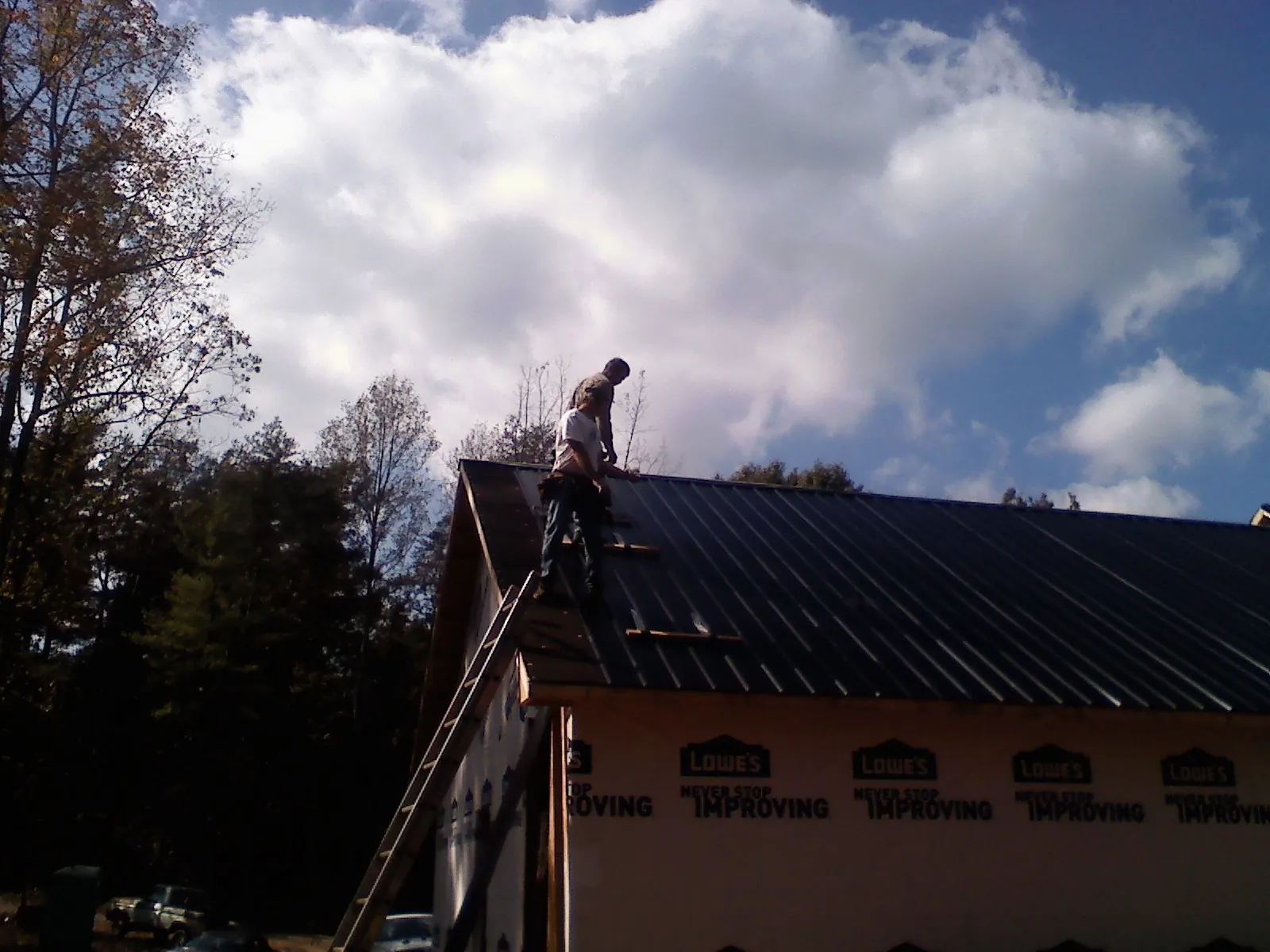 Roofer fastening dark metal panels high against a cloudy sky, from a Roof Inspection job in Thorndale
